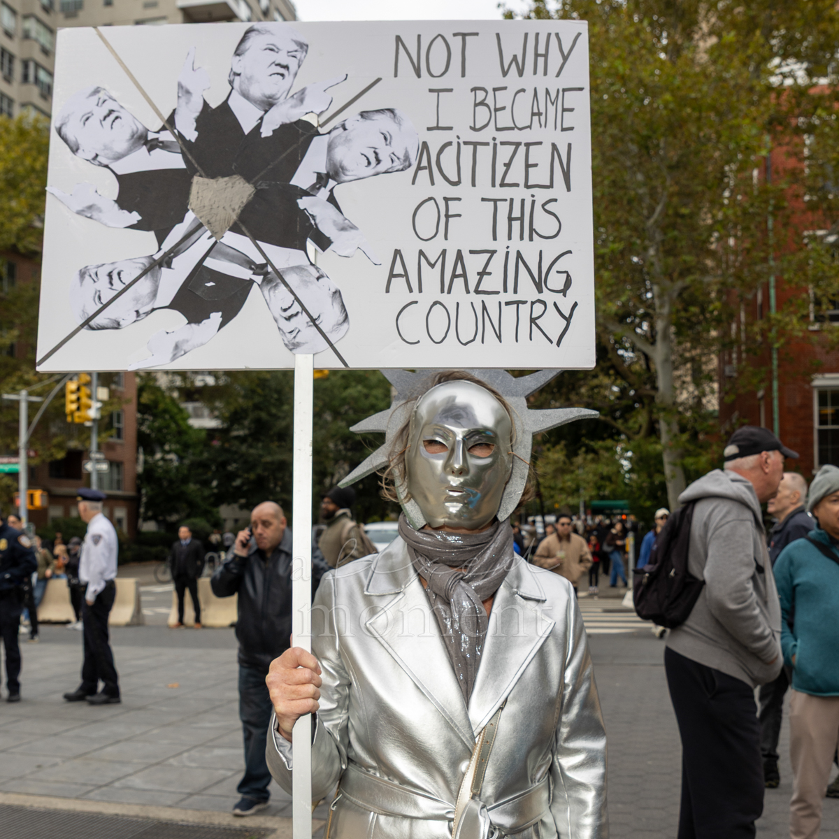 A silver-masked attendee holds a sign expressing criticism of Donald Trump.