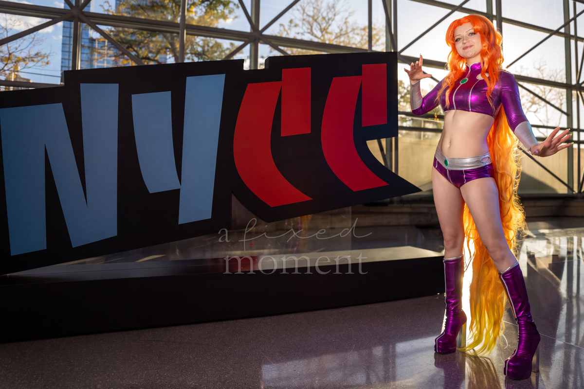 Starfire cosplayer posing beside the NYCC sign at New York Comic Con 2026