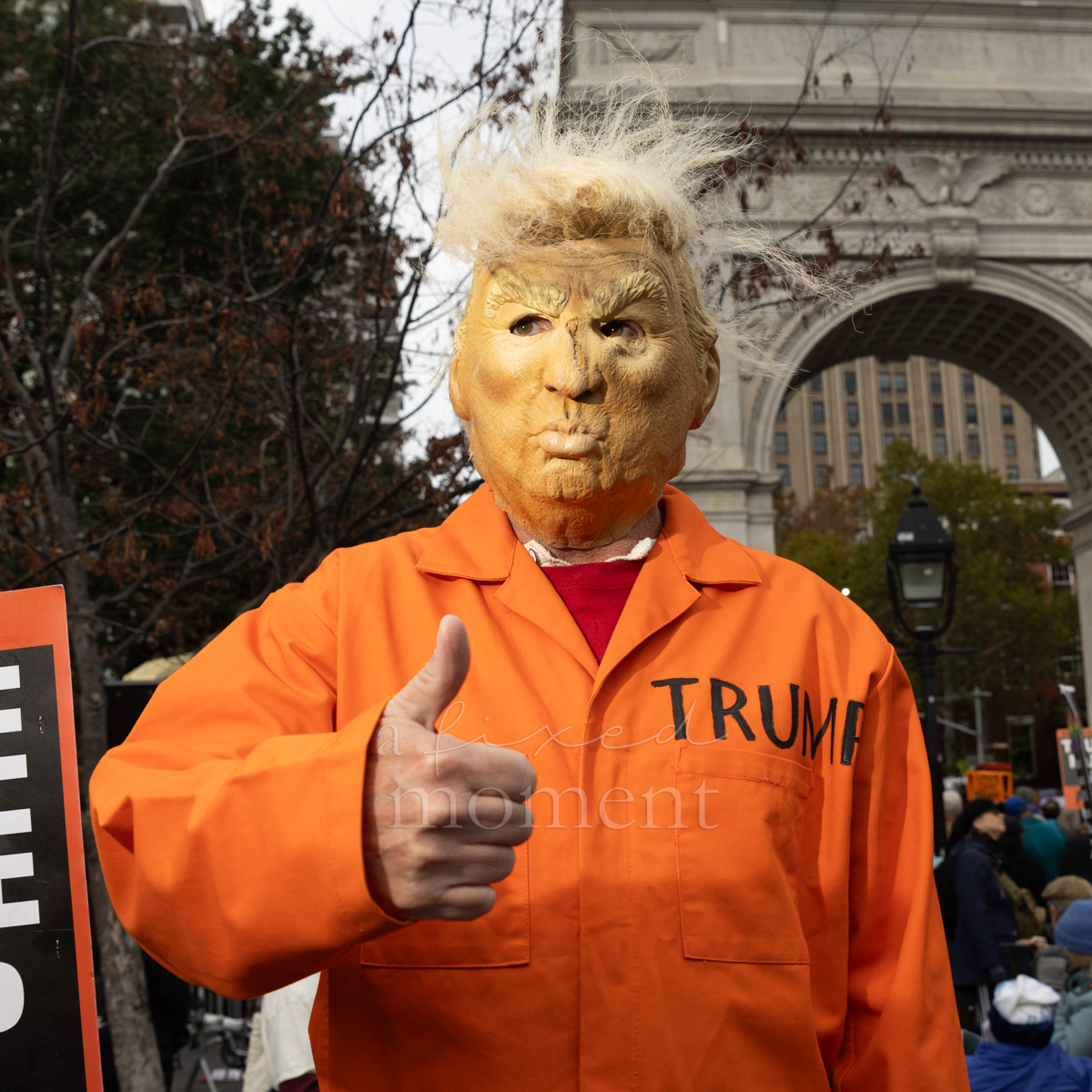 An attendee wears a Trump caricature mask and orange jumpsuit.