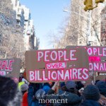 A sea of protest signs fills the street as demonstrators at the 50 50 1 march in New York City on February 17, 2025, raise cardboard placards reading "PEOPLE OVER BILLIONAIRES" in bold red and white lettering. The message, repeated across multiple signs, highlights the protest's stance against wealth inequality and corporate influence in politics.
The crowd, dressed in warm winter clothing, including hats, scarves, and jackets, actively marches through the city. The shot is taken from within the demonstration, showing a dense group of protesters raising their voices and signs in unison. Leafless trees, red-brick buildings, and modern high-rises frame the background, with a traffic light hanging above the march, indicating their movement through the streets of Manhattan.
The 50 50 1 march, which began at Union Square and ended at Washington Square Park, gathered activists advocating for economic justice, wealth redistribution, and government accountability. The powerful visual of repeated messages emphasizes a collective demand for change.