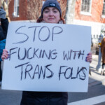 A demonstrator at the 50 50 1 march in New York City on February 17, 2025, stands firmly holding a large handwritten sign that reads: "STOP F*ING WITH TRANS FOLKS."** The message is written in bold black marker, making a clear statement against discrimination and policies targeting transgender individuals.
The protester wears a gray North Face beanie, a black winter coat, and lavender-colored pants. Her expression is serious and determined as she looks at the camera. She has blue-painted nails and holds the sign with both hands, standing in front of a red-brick building. Other demonstrators, some wearing winter clothing, are visible in the background holding their own signs as part of the protest, which began at Union Square and marched to Washington Square Park.
This moment reflects the broader advocacy within the march, which focused on social justice, LGBTQ+ rights, and political activism, reinforcing the demand for equality and protection for marginalized communities.