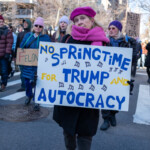 A protester at the 50 50 1 march in New York City on February 17, 2025, holds a vibrant sign that reads: "NO SPRINGTIME FOR TRUMP AND AUTOCRACY" in bold blue and yellow lettering, accompanied by musical notes. The phrase is a reference to Springtime for Hitler, a satirical song from The Producers, used here to critique Donald Trump and authoritarian governance.
The protester is dressed in a fuchsia beret, a matching bright pink scarf, and a black winter coat, standing out in the crowd. Her determined expression and strong grip on the sign reinforce her message. Behind her, fellow demonstrators in winter clothing, including knit hats, sunglasses, and gloves, march forward carrying various protest signs. Some of these signs read "FELON" and "NEVER ADJUST TO EVIL", adding to the political and social justice themes of the demonstration. The urban backdrop features leafless trees, high-rise buildings, and traffic signals, emphasizing the winter setting in Manhattan.
The 50 50 1 march, which began at Union Square and ended at Washington Square Park, was a demonstration advocating for democracy, political accountability, and resistance to authoritarianism.