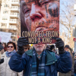A demonstrator at the 50 50 1 march in New York City on February 17, 2025, holds a striking protest sign featuring an edited image of Donald Trump's face merged with a ten-dollar bill. The sign includes the bold text: "CONVICTED FELON, NOT A KING." This powerful visual commentary criticizes Trump's political influence and legal troubles.
The protester, a man with white hair and facial stubble, wears a blue winter coat with a plaid scarf and black gloves as he firmly holds the sign above his face. The crowd of demonstrators behind him, bundled in winter clothing, holds various signs supporting democracy, justice, and resistance against authoritarianism. The protest takes place on a city street lined with high-rise buildings, highlighting the urban setting of the march from Union Square to Washington Square Park.
This image encapsulates the spirit of political activism, emphasizing accountability and the belief in democratic values.