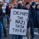 A protester at the 50 50 1 march in New York City on February 17, 2025, holds a bold, handwritten sign reading "DEPORT THE NAZI DATA THIEF." The man is wearing a black face mask, glasses, a dark jacket, and blue jeans as he stands amid a crowd of demonstrators. The background features other protesters holding signs, including one that says "THE WORLD IS WATCHING," with individuals in winter coats, hats, and masks. The setting is a New York City street lined with red brick buildings and bare trees, indicative of the winter season.
This demonstration focuses on political accountability, data privacy, and opposition to authoritarianism, with participants voicing concerns over government policies and corporate influence.