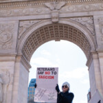 A demonstrator at the 50 50 1 march in New York City on February 17, 2025, stands under the Washington Square Arch, holding a bold protest sign reading:
"VETERANS SAY NO TO FASCISM"
Additional hashtags and messages include #AntiWar, #FightForDemocracy, and other activist-related phrases.
The protester is dressed in a black coat, black gloves, a white beanie, and sunglasses, projecting a strong and determined stance. Their left hand grips a newspaper tucked into their coat, while their right hand holds the sign high.
The Washington Square Arch, commemorating the centennial of George Washington’s inauguration, serves as a symbolic backdrop, reinforcing the message of democracy and resistance against authoritarianism. Below, a large crowd of protesters carries various signs, including one that says "RESIST." The clear blue sky and natural sunlight illuminate the scene, emphasizing the energy and urgency of the demonstration.