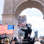 A demonstrator stands elevated, raising a sign that reads:
"THEY LIED AND SENT ME TO FIGHT TERRORISTS ABROAD, WHILE FASCISTS FLOURISHED AT HOME!" during the 50 50 1 march on February 17, 2025, in New York City. The sign's bold typography and strong message highlight concerns about government actions and domestic extremism.
The protester is wearing a black winter coat, gray beanie, sunglasses, and gloves, ensuring warmth during the demonstration. The Washington Square Arch serves as a striking backdrop, emphasizing the historical and civic significance of the location. In the foreground, an American flag waves among the crowd, reinforcing themes of patriotism and activism. Additional signs with messages of truth and resistance can be seen throughout the gathered demonstrators.
This image encapsulates the energy of civic participation, as individuals rally to voice their concerns about democracy, justice, and accountability.