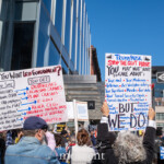 At the Picket Tesla protest on March 1, 2025, outside the Tesla Showroom at 860 Washington Street, NYC, demonstrators hold large, detailed signs listing grievances against Elon Musk, Donald Trump, and government deregulation. One sign, titled "So, You Want Less Government?", contrasts calls for fewer regulations with consequences like outbreaks, plane crashes, corruption, and failing infrastructure. Another sign, labeled "Trump/Musk STOP THE GOVT PURGE", lists vital services at risk, such as Medicare, veterans' aid, consumer protections, and fair wages. The crowd, consisting of activists from Rise and Resist NYC (@riseandresistnyc), holds additional placards denouncing corporate greed and government cutbacks.
The glass exterior of the Tesla showroom reflects the bright blue sky, while the crowd, many wearing hats and jackets, actively participates in the demonstration. The One Way street sign and modern urban architecture frame the scene, reinforcing the protest’s direct opposition to power structures in a commercial hub. The protest reflects broader concerns about billionaire influence, political corruption, and social justice.