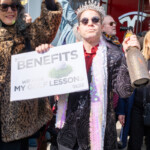 At the Picket Tesla protest on March 1, 2025, outside the Tesla Showroom at 860 Washington Street, NYC, demonstrators stage a satirical performance critiquing billionaire privilege and government policies favoring the wealthy. A man dressed in an extravagant black sequined jacket, wearing a crown and round sunglasses, holds a sign that reads, “Your Benefits Will Fund My Golf Lessons”, with "Trillionaires for Trump" written beneath it. Around his neck, he wears a long iridescent scarf resembling luxury fashion accessories, while in his other hand, he holds a glitter-covered champagne bottle, symbolizing excess and wealth.
Next to him, a protester in a leopard-print faux fur coat and sunglasses raises another sign, further reinforcing the message. The Tesla showroom’s red doors and logo are visible in the background, juxtaposing the theme of corporate and elite wealth. The satirical approach of the demonstrators mocks the extreme economic divide, portraying how government policies disproportionately benefit the ultra-rich while impacting working-class individuals.