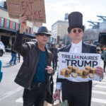 At the Picket Tesla protest on March 1, 2025, at 860 Washington Street, NYC, two demonstrators take part in a satirical performance criticizing corporate greed and economic disparity. The man on the left wears a black leather jacket, blue shirt, and sunglasses, holding a handmade sign reading:
"Let them EAT CAKE! Trillionaires for Trump,"
a reference to Marie Antoinette’s infamous (though disputed) quote, used here to mock out-of-touch elites.
Beside him, a man dressed as a wealthy aristocrat, wearing a black tailcoat, white bowtie, and top hat, holds a sign that reads:
"Trillionaires for Trump," with stacks of gold coins.
The Whole Foods shopping bag he carries adds another layer of irony, playing into the theme of wealth disparity and high living costs. The background captures an urban protest scene with activists marching, holding signs, and engaging in the demonstration against Elon Musk’s corporate influence and policies. The protest was organized by Rise and Resist NYC (@riseandresistnyc).