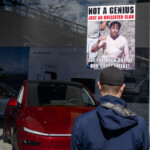 At the Picket Tesla protest organized by Rise and Resist (@risenresistnyc) on March 1, 2025, outside the Tesla Showroom in Manhattan (860 Washington Street, NYC), a protester stands facing the glass window of the showroom, where a sign is taped. The sign features an edited image of Elon Musk shirtless, with the bold message:
"NOT A GENIUS"
"JUST AN UNELECTED SLOB"
"GET THE HECK OUT OF OUR GOVERNMENT!"
The protester, seen from behind, wears a dark blue hooded jacket and a black baseball cap, observing the sign placed against the showroom's glass. The reflection of the sky and buildings can be seen in the glass, along with the interior of the Tesla showroom, where a sleek red Tesla vehicle is prominently displayed. A showroom sign inside reads "Go Anywhere," contrasting sharply with the protest message.
To the right of the protester, another sign from Rise and Resist is partially visible, continuing the theme of anti-Musk criticism. The demonstration is part of a broader movement opposing billionaires' influence over government and corporate accountability.