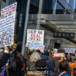 A large crowd gathers outside the Tesla Showroom at 860 Washington Street, NYC, during the Picket Tesla protest organized by Rise and Resist (@risenresistnyc) on March 1, 2025. Protesters hold up a variety of handmade signs condemning billionaire power, political influence, and threats to social programs.
One of the most prominent signs in the image, held high on a white poster board with blue and red text, reads:
"TRUMP/MUSK STOP THE GOVT PURGE"
Below this, it lists various social services at risk, including:
"Your mail,"
"Your Medicare,"
"Veterans' aid,"
"Workplace safety,"
"Your Social Security check,"
"Tainted food,"
"Fairness"
The sign emphasizes "BUY LIES. DO FASCISM."
Another large sign in the center reads:
"STOP THE REAL STEAL"
"(OF OUR Safety! Civil Rights! Consumer Protections! Productive Freedom! Veterans Support! And More!)"
Additional signs in the background amplify the protest's themes, with messages such as:
"THIS BILLIONAIRE IS KILLING OUR GOVERNMENT"
"FASCISM" with an image of Donald Trump
"MUSK OUT OF CONTROL"
The crowd, diverse in age and appearance, is dressed in jackets and scarves, indicating the protest is taking place in cooler weather. Many participants raise their fists or signs, engaged in chanting and discussions. The Tesla showroom's glass facade reflects the cityscape, blending the demonstration with its urban backdrop.
The Rise and Resist (@risenresistnyc) protest highlights growing concerns over billionaire control, corporate greed, and social justice, targeting both Elon Musk and Donald Trump as symbols of unchecked power.