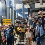 At the Picket Tesla protest organized by Rise and Resist (@risenresistnyc) on March 1, 2025, outside the Tesla Showroom at 860 Washington Street, NYC, demonstrators rally against Elon Musk, corporate greed, and billionaire influence in politics.
The crowd holds a variety of bold protest signs. In the foreground, a protester raises a black and yellow sign that reads:
"MAKE NO MISTAKE THIS IS A COUP."
To the right, another demonstrator in a yellow jacket and sunglasses holds a sign stating:
"OVERTHROW THE OLIGARCHS"
with images of Elon Musk, Mark Zuckerberg, and Donald Trump, highlighting concerns over their outsized power.
In the center, activist Jay W. Walker raises a sign that repeatedly states "NAZI" alongside an altered image of Elon Musk, drawing stark comparisons. Wearing a quilted blue jacket, sunglasses, and a cap covered in protest buttons, he gestures while chanting. Another protester nearby holds a sign that reads:
"THIS IS THE IMMIGRANT WHO TOOK YOUR JOB."
Additional signs in the background reinforce the protest’s message:
"RESIST THE MUSK-TRUMP COUP"
"DEFUND MUSK" (handwritten on a whiteboard)
"BOYCOTT TESLA" with an American flag
A large cardboard cutout of Elon Musk in a black-and-white suit, posing with his arm raised, stands at the edge of the protest, visually reinforcing the demonstrators' accusations.
The Rise and Resist (@risenresistnyc) protest reflects the group’s commitment to economic justice, corporate accountability, and resistance to the growing influence of billionaires in government and business. The Tesla showroom’s reflective glass mirrors the activists and their signs, merging corporate and protest imagery into a single frame.