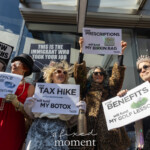 At the Picket Tesla protest organized by Rise and Resist (@risenresistnyc) on March 1, 2025, outside the Tesla Showroom at 860 Washington Street, NYC, a group of demonstrators dressed as wealthy elites use satire and theatricality to highlight economic injustice and billionaire greed.
The four central protesters, dressed in luxurious faux fur coats, sequins, pearls, tiaras, and sunglasses, hold up mock campaign-style signs with sarcastic messages about how the wealthy benefit from economic inequality:
"YOUR POST OFFICE CLOSURE WILL FUND MY SPACE ADVENTURE"
"YOUR TAX HIKE WILL FUND MY BOTOX"
"YOUR PRESCRIPTIONS WILL FUND MY BIRKIN BAG"
"YOUR BENEFITS WILL FUND MY GOLF LESSONS"
One protester in a red dress, black hat, pearl necklace, and opera gloves dramatically holds the "Space Adventure" sign, referencing Elon Musk’s involvement in SpaceX and government contracts. Another activist in a white ruffled outfit and sunglasses clutches the "Tax Hike for Botox" sign. A demonstrator in a leopard-print coat raises her gold-glittered champagne bottle prop while holding the Birkin Bag sign. On the right, a protester in a sequin-covered suit, tiara, and pink feather boa grins while displaying the Golf Lessons sign.
Surrounding them, other demonstrators hold anti-Musk and anti-oligarchy signs, including:
"OVERTHROW THE OLIGARCHS" with images of Elon Musk, Donald Trump, and Mark Zuckerberg
"THIS IS THE IMMIGRANT WHO TOOK YOUR JOB"
The Tesla showroom's sleek glass exterior reflects the crowd, merging the corporate and activist spaces. The bright sunlight enhances the dramatic and satirical nature of the protest, making the message visually striking.
The Rise and Resist (@risenresistnyc) demonstration uses humor, performance, and powerful visuals to critique billionaire wealth hoarding, corporate greed, and economic policies that disproportionately impact everyday people.