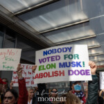 At the Picket Tesla protest organized by Rise and Resist (@risenresistnyc) on March 1, 2025, outside the Tesla Showroom at 860 Washington Street, NYC, demonstrators raise bold, colorful signs opposing Elon Musk’s influence, corporate power, and cryptocurrency schemes.
A large sign with multicolored text reads:
"NOBODY VOTED FOR ELON MUSK! ABOLISH DOGE"
This statement critiques Musk’s growing political and economic influence while calling for the abolition of Dogecoin, a cryptocurrency he has frequently promoted and manipulated.
Other visible signs in the crowd include:
"Say NO! to Tesla and to Kings", equating Musk’s power to monarchical rule.
"HEY ELON! Why fly to Mars when your head’s already up Uranus?", a humorous jab at his space ambitions.
"YOU already make bad trucks, why make bad governments?", likely referencing Tesla’s Cybertruck and Musk’s political moves.
The diverse crowd, wearing red jackets, sunglasses, and patriotic-themed accessories, passionately raises their signs. A protester wearing a red hat and an American flag scarf stands in the background, reinforcing the political weight of the demonstration.
This protest, led by Rise and Resist (@risenresistnyc), reflects broader concerns over corporate overreach, billionaire power, and Musk’s unchecked influence on politics, technology, and finance.