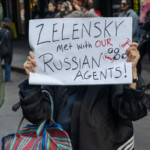 At the Picket Tesla protest outside the Tesla Showroom at 860 Washington Street, NYC, on March 1, 2025, a demonstrator stands with a handwritten sign that reads "Zelensky met with OUR Russian Agents!", with additional handwritten notations referencing Vance and Trump. The individual, whose face is partially obscured by the sign, is wearing a black coat and carrying a large striped bag.
The background shows a gathering of protesters and onlookers, some capturing the event on their phones, while others stand observing. The location is framed by the brick architecture of Manhattan’s Meatpacking District, an area known for its mix of commercial spaces and high-end retail, contrasting with the grassroots activism taking place. The message on the sign suggests a critique of political relationships and influence, aligning with the broader themes of the demonstration against corporate and political power consolidation.