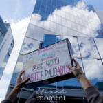 At the Picket Tesla protest outside the Tesla Showroom at 860 Washington Street, NYC, on March 1, 2025, a demonstrator raises a handmade sign against the backdrop of towering glass buildings reflecting the partly cloudy sky. The sign, written in colorful text, lists essential services such as "HEALTH CARE, EDUCATION, NUCLEAR TECHNICIANS, AIR TRAFFIC CONTROLLERS, VETERANS, CONSUMER PROTECTION, HOUSING, and DIPLOMACY", followed by the bold statement "ARE NOT WASTE, FRAUD, ABUSE!"
The message challenges narratives that frame government-funded programs as excessive spending, instead emphasizing their critical role in society. The protest, part of a broader demonstration against Elon Musk, corporate overreach, and economic inequality, gathered activists advocating for corporate accountability and protection of public resources.
The framing of the image, taken from below, emphasizes the power and urgency of the demonstrator’s message, contrasting the grassroots protest with the towering corporate structures above.
