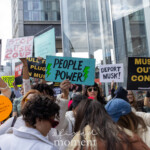 A large group of protesters gathers outside the Tesla Showroom at 860 Washington Street, NYC, on March 1, 2025, for the Picket Tesla protest, organized by Rise and Resist (@riseandresistnyc). The demonstrators hold up an array of bold, attention-grabbing signs, each conveying strong messages against Elon Musk, corporate greed, and political influence by billionaires.
One of the most prominent signs, painted in bright blue with green lightning bolts, declares "People Power!", symbolizing the grassroots energy of the protest. Other notable signs include "Stop Musk Coup," "Deport Musk!", "Pull the Plug on Musk," and "Musk Out of Control", reflecting the frustration of those in attendance. Another protester raises a sign that satirically reads, "Goes from 0 to 1939 in 3 seconds – Tesla: The Swasticar," drawing a historical parallel in critique of Musk’s influence.
The crowd is highly engaged, chanting and raising their voices, while some individuals play instruments, adding to the spirited resistance. Protesters wear sunglasses, hats, and scarves, while a few capture the moment on their phones and cameras. The atmosphere is one of defiant energy and unified purpose, calling for action against what they see as unchecked corporate power and political manipulation.