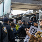 At the Picket Tesla protest outside the Tesla Showroom at 860 Washington Street, NYC, on March 1, 2025, a protester is being escorted by NYPD officers into a police van as fellow demonstrators look on. Several NYPD officers in uniform, including members of the Strategic Response Group, are seen managing the arrest and controlling the crowd. In the foreground, a protester in a leopard-print coat holds a "Billionaires for Trump" sign, while another sign in the background reads "Hey Elon, Quit Using Our Country as a Playground."
Spectators watch from an elevated walkway above the scene, highlighting the public attention and support for the protest. The event, organized by Rise and Resist NYC (@riseandresistnyc), aimed to call out corporate power, demand accountability, and push back against Elon Musk's influence in politics and business.