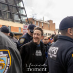 A protester wearing a black sweatshirt with Spanish text reading "No Nos Quedaremos Callados" ("We Will Not Stay Silent") is escorted by NYPD officers from the Strategic Response Group during the Picket Tesla protest outside the Tesla Showroom at 860 Washington Street, NYC, on March 1, 2025. Despite the circumstances, the individual appears calm and smiling, surrounded by police officers in navy blue uniforms with "NYPD Strategic Response Group" patches on their sleeves.
In the background, fellow protesters continue chanting and holding up signs, including one that reads "Hey Elon, Why Fly to Mars When Your Head's Already Up Uranus?", demonstrating the bold messaging and humor used during the protest. Crowds of demonstrators and onlookers document the moment with their phones, capturing the police action and the protester’s defiant expression.
This protest, organized by Rise and Resist NYC (@riseandresistnyc), called out corporate power, economic inequality, and Elon Musk’s influence in politics.