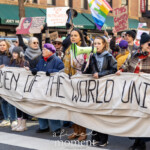 Activists Leslie Cagan, Yanery Cruz, Evie K, and Kim Russell lead a large, determined group of protesters during the Women's March held on March 8th, 2025, marching from Washington Square Park toward Union Square in New York City. Together, they carry a prominent, handmade banner with bold lettering that reads:
"WOMEN OF THE WORLD UNITE!"
Evie K passionately speaks through a green megaphone, rallying the marchers and energizing the crowd, while Leslie Cagan and Yanery Cruz walk steadily and confidently alongside, guiding the demonstration. Kim Russell enthusiastically raises a fist in solidarity, embodying the spirit of activism and unity.
Participants behind the leaders hold numerous vibrant signs, including a rainbow flag symbolizing LGBTQ+ inclusion, and protest placards with feminist messages such as "F*ck the Patriarchy" and "This Country is a Dumpster Fire." The atmosphere is spirited and resolute, with demonstrators dressed warmly in coats, hats, and scarves, marching peacefully yet powerfully through the city streets.