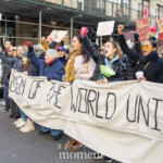 Activists Leslie Cagan, Yanery Cruz, Evie K, and Kim Russell lead a large, determined group of protesters during the Women's March held on March 8th, 2025, marching from Washington Square Park toward Union Square in New York City. Together, they carry a prominent, handmade banner with bold lettering that reads:
"WOMEN OF THE WORLD UNITE!"
Evie K passionately speaks through a green megaphone, rallying the marchers and energizing the crowd, while Leslie Cagan and Yanery Cruz walk steadily and confidently alongside, guiding the demonstration. Kim Russell enthusiastically raises a fist in solidarity, embodying the spirit of activism and unity.
Participants behind the leaders hold numerous vibrant signs, including a rainbow flag symbolizing LGBTQ+ inclusion, and protest placards with feminist messages such as "F*ck the Patriarchy" and "This Country is a Dumpster Fire." The atmosphere is spirited and resolute, with demonstrators dressed warmly in coats, hats, and scarves, marching peacefully yet powerfully through the city streets.