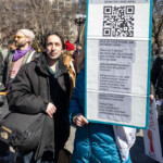 A protester at the Women's March on March 8, 2025, in Union Square, New York City, holds a large sign featuring a QR code with a call to action for voter mobilization. The sign reads:
"SCAN FOR MORE INFO!
PICK UP YOUR PHONE AND DO SOMETHING!
There are 2 special elections April 1st in Florida and 1 in New York - TBD and we need help!
Special election turnout is always lower than the general elections.
Did you know on Jan. 28th a Democrat just flipped a solid red Missouri seat moving a district that voted for Trump by a large margin?
Support the special election turnout by:
DONATING
CALL BANKING!
POSTCARD WRITING!
SPREADING THE WORD!"**
The protester holding the sign is wearing a blue puffer jacket, and their face is partially obscured by the sign. Next to them, another individual in a black coat with long dark hair looks directly at the camera with a neutral expression. Several other protesters can be seen in the background, some wearing pink hats and holding additional signs advocating for women's rights and democracy. The event is taking place in a lively setting with leafless trees and statues in the background, capturing the essence of a grassroots movement aimed at political engagement.
