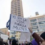 At the Women's March 2025 in Union Square, NYC, a protester holds up a handmade sign written in Spanish that reads:
"Yo soy la vida, fuerza, mujer."
(Translation: "I am life, strength, woman.")
The demonstrator, wearing a maroon jacket and a purple beanie, firmly holds the sign high, making their message visible against the backdrop of New York City's urban skyline and commercial buildings. Other protesters are visible in the crowd, many wearing hats, scarves, and sunglasses as they participate in the march. The sign, written in bold black letters on white poster board, expresses a powerful statement of resilience and empowerment for women.
The event is filled with people from diverse backgrounds advocating for gender equality, reproductive rights, and women's empowerment, with signs in multiple languages emphasizing the global nature of the feminist movement.