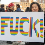 At the Women's March 2025 in Union Square, NYC, a protester holds a striking sign with the word "FUCK!" written in bold rainbow-striped letters, symbolizing LGBTQ+ pride and resistance. The woman, with long dark hair and a black jacket, stands confidently, her expression serious and determined as she displays the statement in the middle of the demonstration.
To the right, another participant, dressed in a white beanie, glasses, and purple gloves, holds a sign that reads:
"Being trans is already hard enough."
The crowd behind them is filled with diverse marchers, some wearing colorful hats and accessories, all gathered in support of women’s rights, LGBTQ+ rights, and social justice. The atmosphere is lively, with protesters expressing their demands for equality, inclusion, and resistance against discrimination.
The use of rainbow colors on the bold sign emphasizes LGBTQ+ visibility and pride, while the explicit statement reflects frustration, urgency, and defiance against ongoing social and political issues.